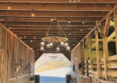 White string lights cascade from exposed beams in a rustic barn reception space where weddings are held in Virginia.